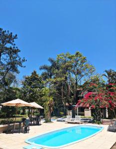 uma piscina com mesas e cadeiras e um guarda-sol em La Remonta Residence em Ipiabas