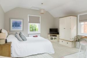 a white bedroom with a large white bed and windows at Stylish and homely 1 bed Edwardian Coach House in Colchester