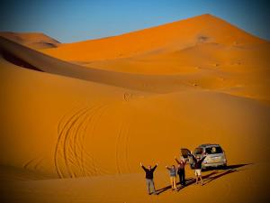 Porte De Sahara Ouzina في Ouzina: مجموعة من الناس تقف في الصحراء مع سيارة فان