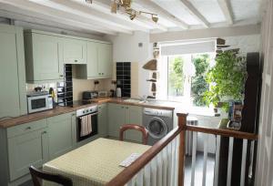 uma cozinha com armários brancos, uma mesa e uma janela em Bluebell cottage em Ulverston