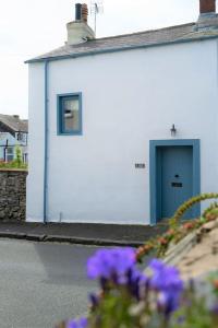 a white building with a blue door and some purple flowers at Bluebell cottage in Ulverston