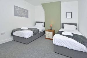 a bedroom with two beds and a wooden nightstand at Croft House - By Sigma Stays in Crewe