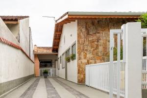 a walkway between two buildings with a white fence at Casa Aconchego - O refúgio perfeito para amar e descansar in Peruíbe
