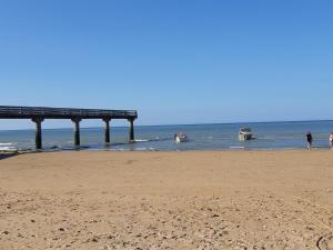 a pier on a beach with people in the water at Grande maison , jardin,flipper,babyfoot, ping pong, 1 km mer, proche golf, Port en Bessin, Bayeux et plages du débarquement, adaptée enfants in Commes