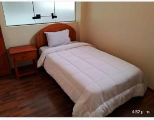 a small bedroom with a white bed and a night stand at Hotel Casa Shami in Cusco