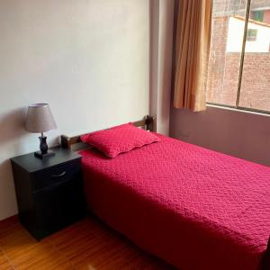 Duplex amoblado en el corazón de Ayacucho في اياكوتشو: غرفة نوم بسرير احمر ومصباح ونافذة