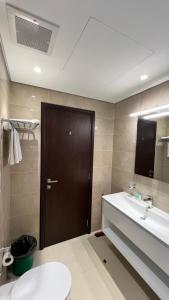 La salle de bains est pourvue de toilettes, d'un lavabo et d'une porte marron. dans l'établissement Hawana salalah Apartment Mimosa, à Salalah