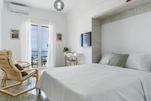 a white bedroom with a bed and a chair at On The Port in Rafina