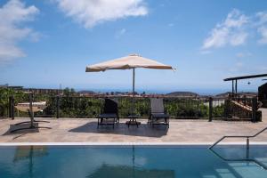 a swimming pool with two chairs and an umbrella at Villa La Graja by Huskalia - private pool in Los Llanos de Aridane