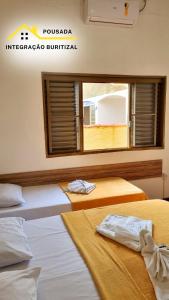 two beds in a room with a window at Pousada Integração Buritizal in Buritizal