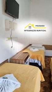 two beds in a room with a tv on the wall at Pousada Integração Buritizal in Buritizal