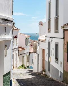 an alley with white buildings and the ocean in the background at Salema Beach Apartment in Salema