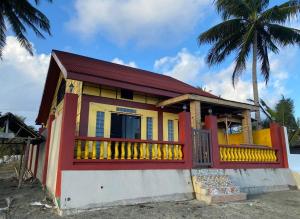 a small yellow and red house with a palm tree at Koa's Beach House in Tangalan