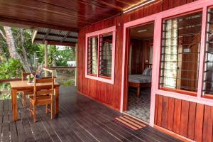 ein rotes Haus mit einer Holzterrasse mit einem Tisch in der Unterkunft Leleana Resort Kolombangara Island 