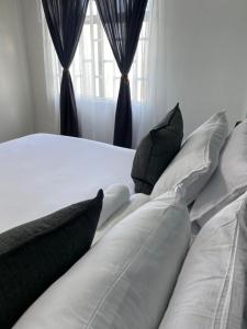 a white bed with black pillows in front of a window at Stylish apartments in Gaborone