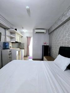 a bedroom with a large white bed and a kitchen at Apt Bassura Studio Tower F w/ Pool, Wi-Fi & Netflx in Jakarta