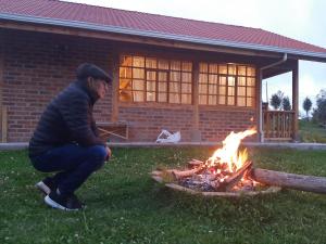 a man squatting next to a fire in a yard at Cabañas Tecla María in Otavalo +6 photos
