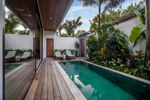 an indoor pool with a wooden deck and a house at Villa Sessun by Alfred in Bali in Canggu