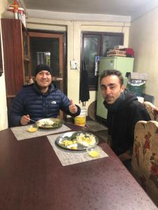 Dois homens sentados numa mesa com pratos de comida. em Samriddhi HomeStay em Kathmandu