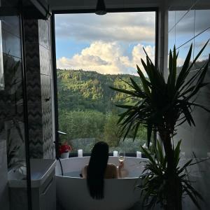 une femme assise dans une baignoire donnant sur une fenêtre dans l'établissement Forest Hub, à Slavsko