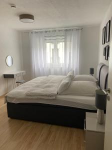 een groot bed in een witte slaapkamer met een raam bij Gemütliches City Apartment in Friedrichshafen