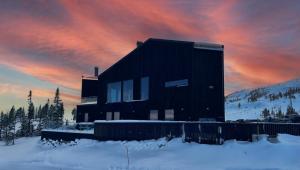 una casa negra en la nieve con una puesta de sol en Trilodge - Unique cabin with high standard, views, ski in & out, attractive location, en Meråker