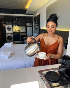 Eine Frau, die eine Tasse Kaffee in einem Hotelzimmer gießt. in der Unterkunft The Capital Mirage in Kapstadt