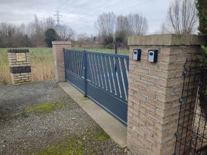a fence with a gate with a brick pillar next to it at Mobil-home Côté Mur in Holque