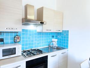 una cucina piastrellata di blu con lavandino e forno a microonde di Attico Ta Rosalba a Porto Azzurro