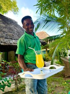 un hombre sosteniendo una bandeja con una bebida. en Green's Nungwi, en Nungwi