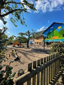 une clôture en face d'une aire de jeux avec un bâtiment dans l'établissement Camping Saint-Lambert - Maeva, à Millau
