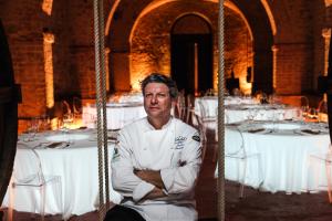 Ein Mann in einer Kochuniform, der vor Tischen sitzt. in der Unterkunft La Locanda Del Capitano in Montone