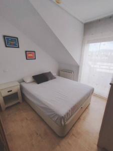 a white bedroom with a bed and a window at Ático de 60 m2 en urbanización privada in Noja