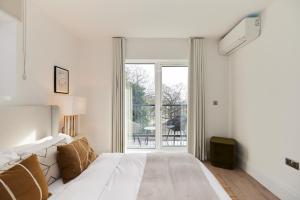 een witte slaapkamer met een bed en een glazen schuifdeur bij The Wembley Park Retreat - Modern 2BDR Flat with Balcony in Londen