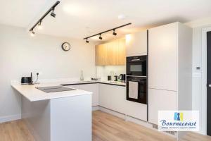 a white kitchen with a counter and a refrigerator at Bournecoast - Brand New Clifftop Apartment with Balcony - FM9574 in Bournemouth