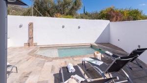een zwembad op een patio met stoelen en een witte muur bij Villa La Fuente Periana by Ruralidays in Periana