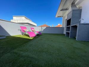 two pink chairs sitting on a balcony with grass at Nênê House - Casa de Praia by Férias em Figueira in Figueira da Foz