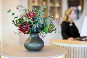 een groene vaas met bloemen op een tafel met een vrouw bij Hotel Odense in Odense