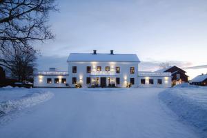 une maison blanche dans la neige avec les lumières allumées dans l'établissement Ulvsby Herrgård, à Sunne