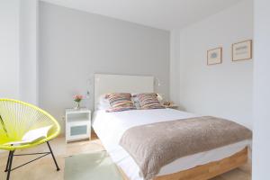 a white bedroom with a bed and a yellow chair at OceanVibe Loft MalagaFlat in Málaga