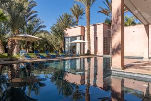einen Pool mit Stühlen, Sonnenschirmen und Palmen in der Unterkunft Luxury 5bed villa with heated pool in Marrakesch