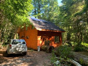 a small wooden cabin with a car parked in front of it at Casa Encantada HuiloHuilo in Puerto Fuy