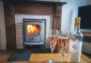 a bottle of wine and two glasses on a table with a fireplace at Min y Don, stone cottage by the edge of the sea, Llangrannog in Llangrannog