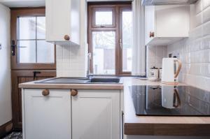 La cuisine est équipée de placards blancs, d'un évier et de fenêtres. dans l'établissement The Brambles - 2 bedroom Cottage - Llanteg, à Pembrokeshire