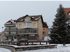 a large building with a tree in the snow at Apartman Oskar 1 in Kupres