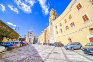 una calle con coches aparcados y una torre del reloj en La Cattedrale Apartments&Suite - Affitti Brevi Italia, en Gravina in Puglia
