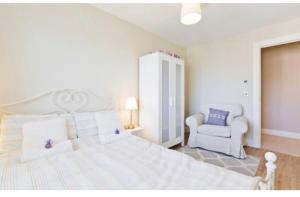 a white bedroom with a large bed and a chair at Modern Homestay 15 minutes to Dublin Airport in Ballyboughal