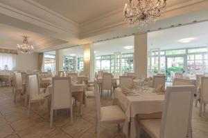 un restaurante con mesas y sillas blancas y una lámpara de araña en Hotel Athena, en Cervia