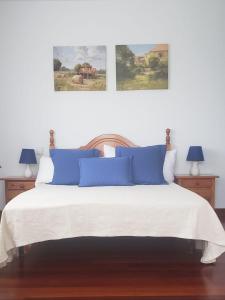 a bed with blue pillows and two paintings on the wall at hospedaje casa milagros in Santillana del Mar