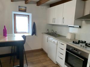 cocina con armarios blancos, mesa y ventana en Le Cantou en Castelnau-de-Mandailles